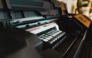 Close-up view of a commercial printer with multiple ink cartridges installed, showing cyan, magenta, yellow, and black color options.