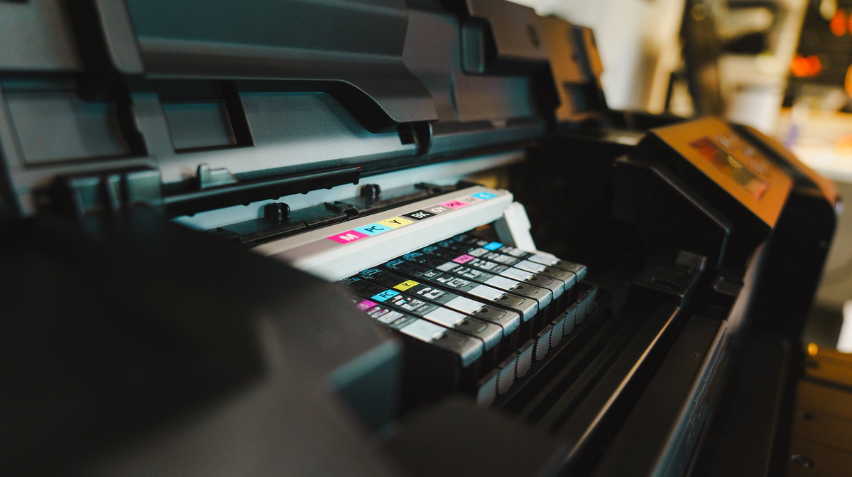 Close-up view of a commercial printer with multiple ink cartridges installed, showing cyan, magenta, yellow, and black color options.