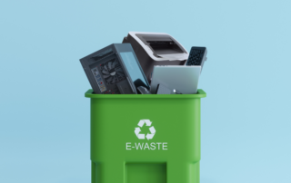 Green recycling bin labeled "E-Waste" filled with discarded electronics, including a printer, computer components, and a keyboard, representing environmentally friendly printer disposal. The image emphasizes responsible e-waste recycling.