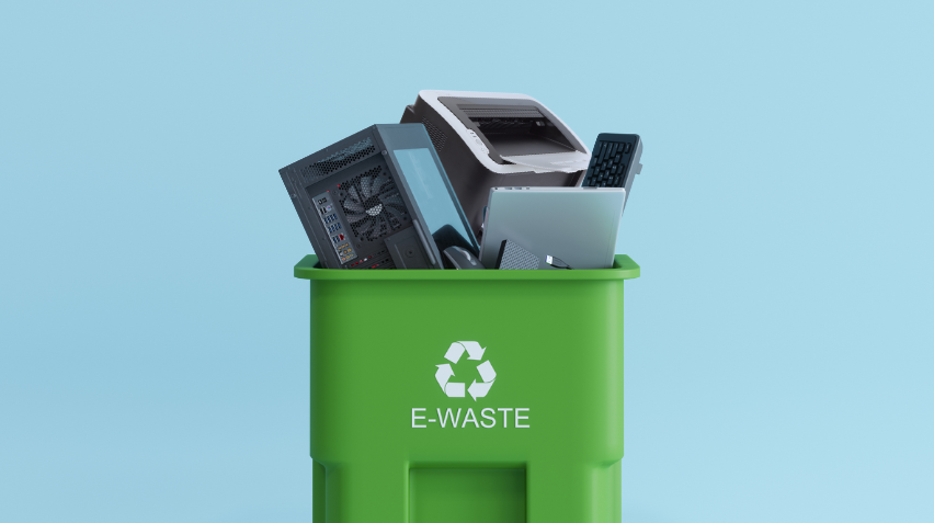 Green recycling bin labeled "E-Waste" filled with discarded electronics, including a printer, computer components, and a keyboard, representing environmentally friendly printer disposal. The image emphasizes responsible e-waste recycling.