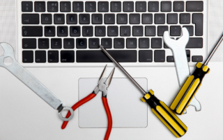 A laptop keyboard with various tools, including pliers, wrenches, and screwdrivers, placed on top, symbolizing office equipment maintenance.